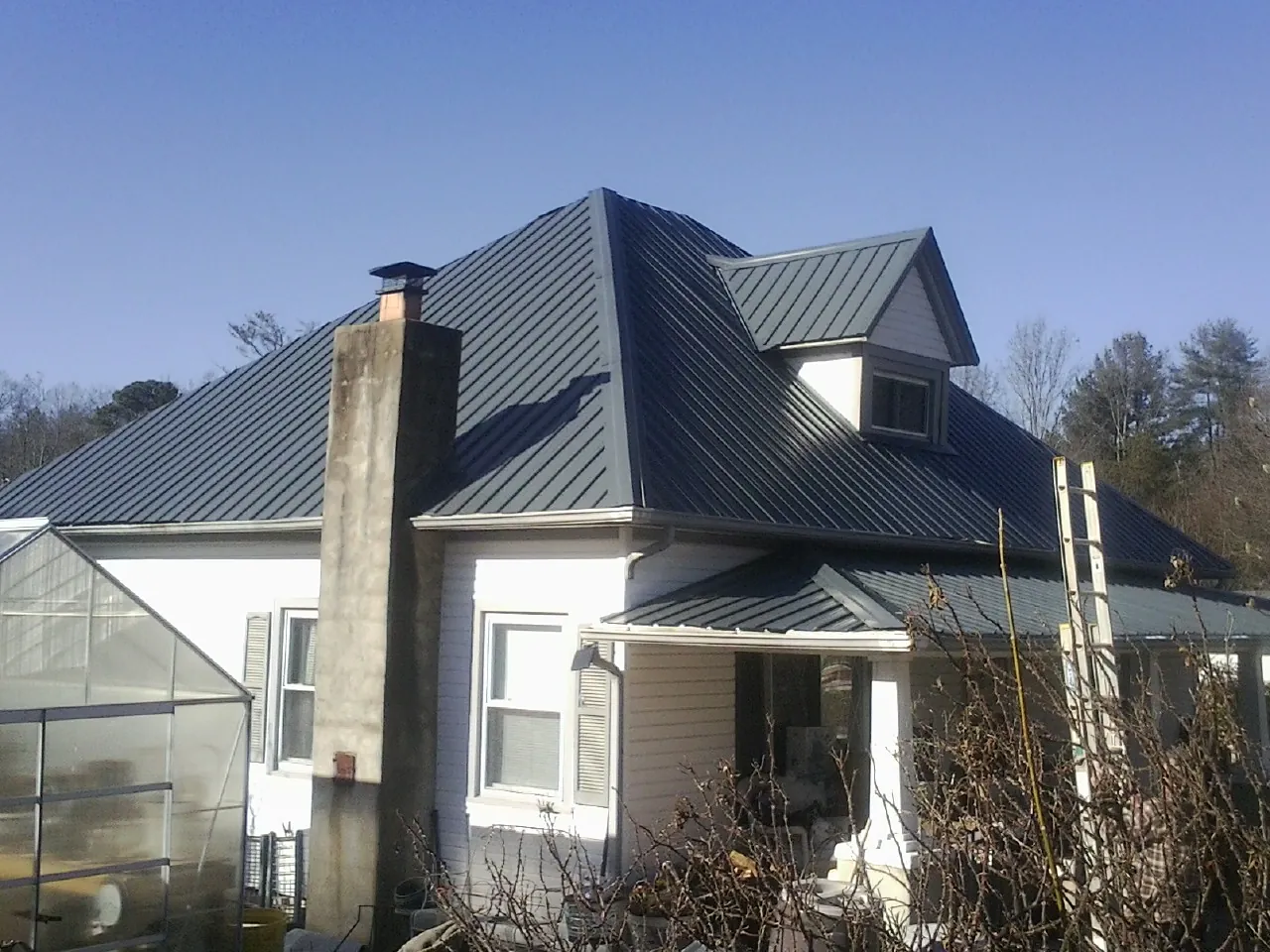 Dark blue standing seam metal roof on a white farmhouse with dormer — Slate & Tile Roof Repair by Roofing Brothers in Eldridge