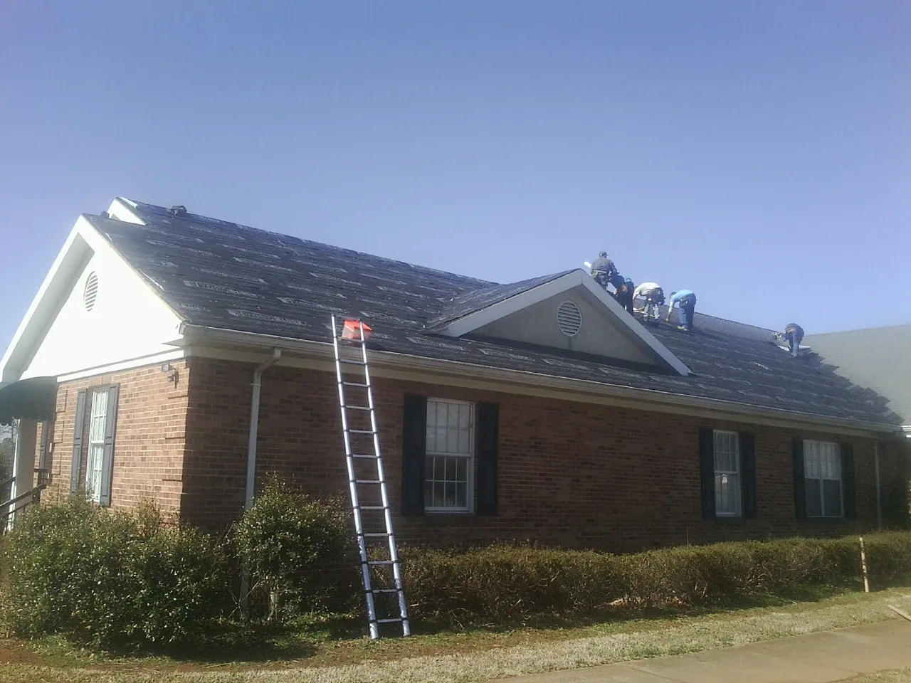 Crew tearing shingles off a brick ranch roof with a ladder set — Metal Roof Repair work by our crew in Eldridge
