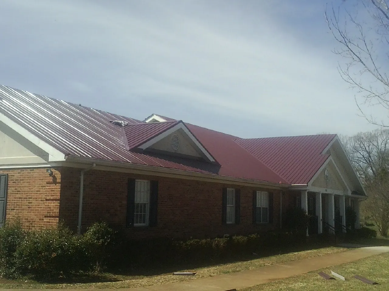 Red metal roof with gabled entries on a long brick building, from a Hail Damage Roof Repair job in Eldridge