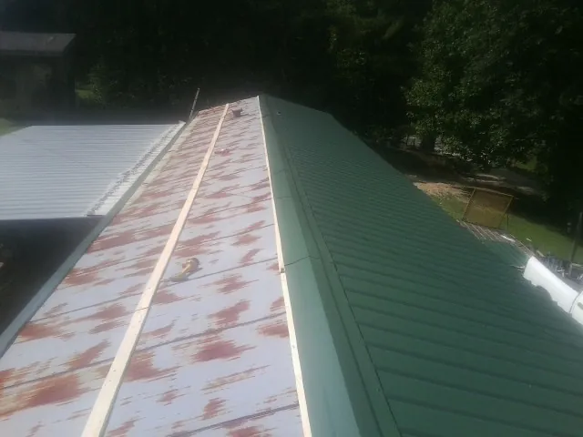 Old rusted panels beside newly installed green metal roofing — Wind Damage Roof Repair by Roofing Brothers in Eldridge