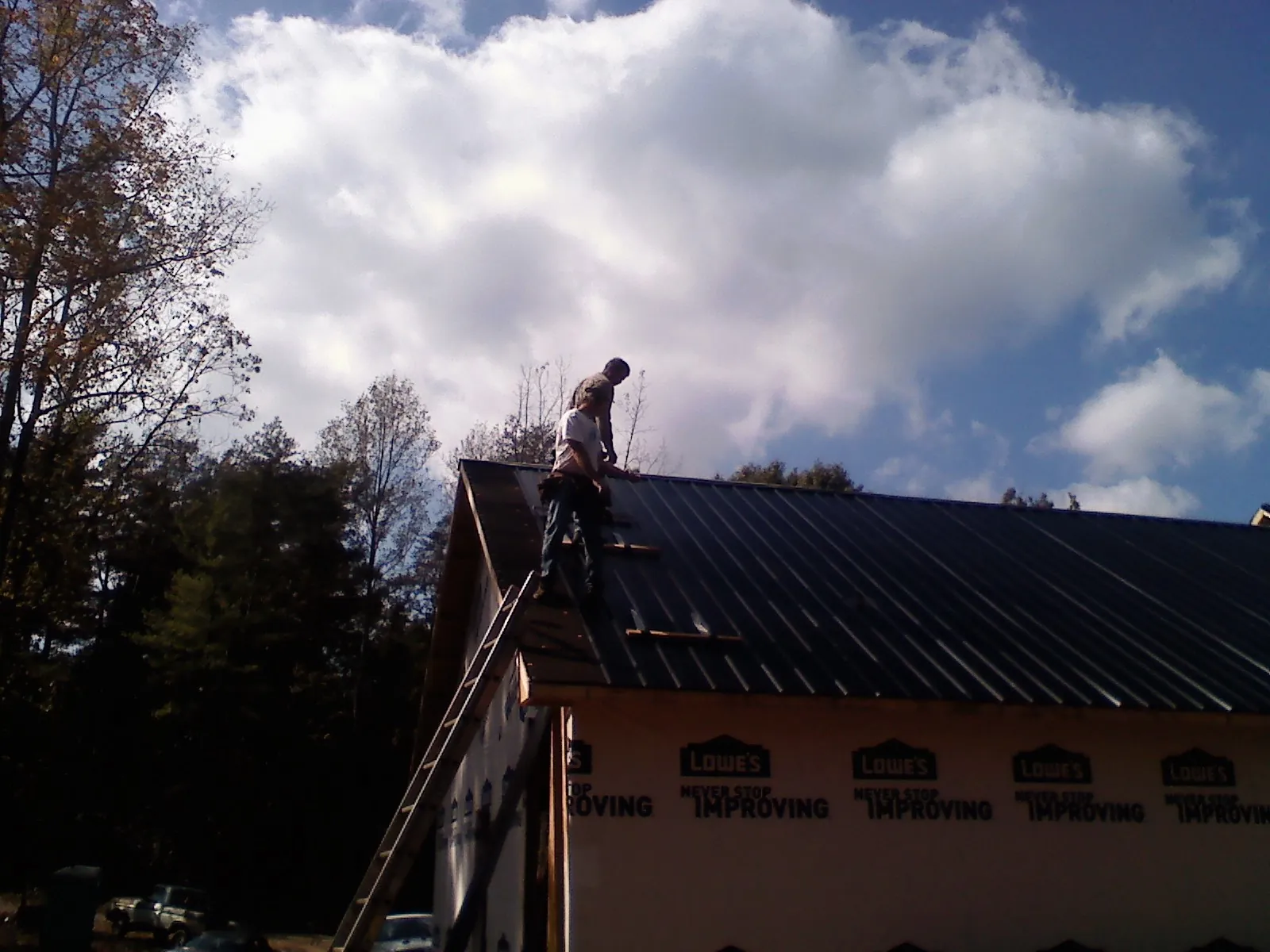 Roofer fastening dark metal panels high against a cloudy sky, from a Roof Inspection job in Eldridge