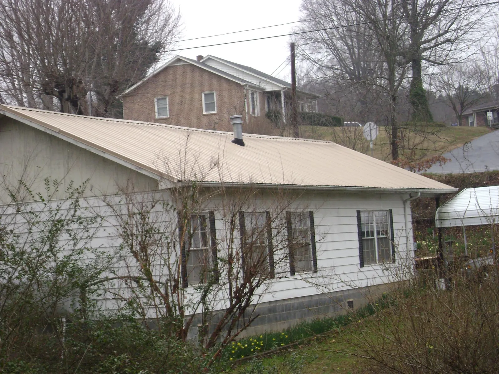 Tan metal roof on a white sided house set into a hillside — Commercial Roofing by Roofing Brothers in Eldridge