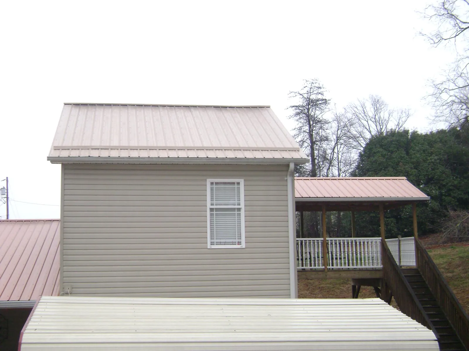 Tan metal roofs on a two story addition and attached porch, from a Roof Replacement job in Eldridge
